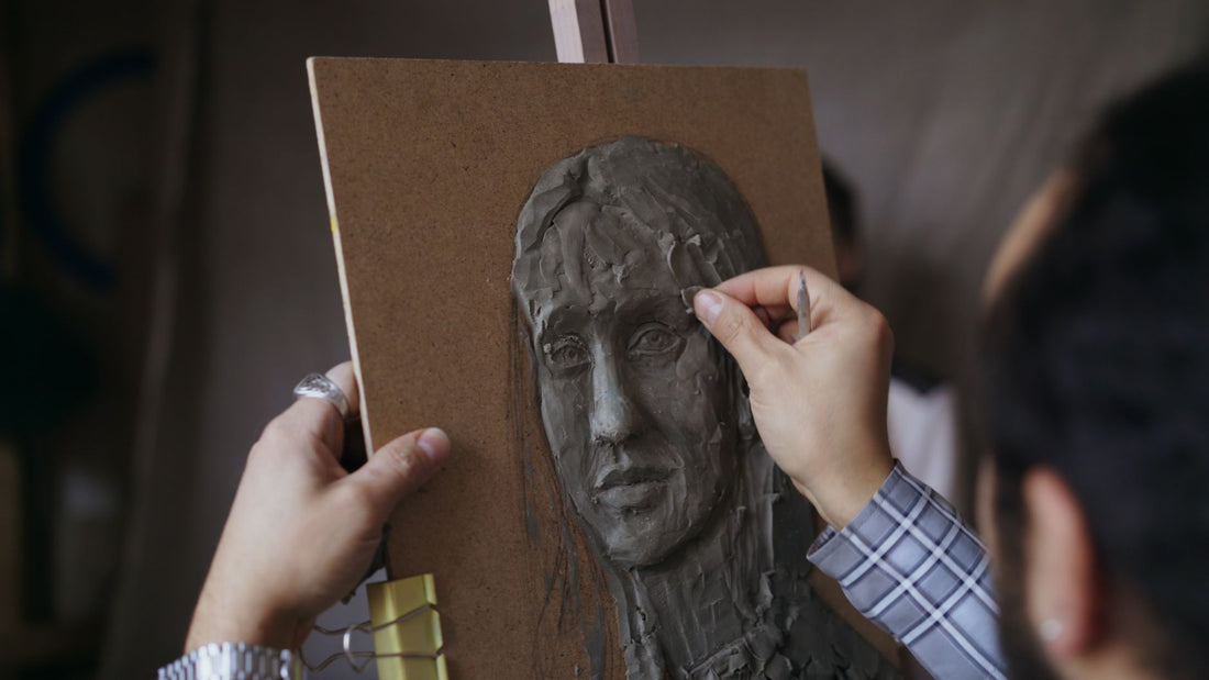 Hands shaping a small clay model in a sculptor's studio