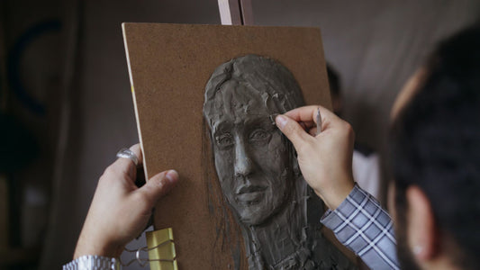 Hands shaping a small clay model in a sculptor's studio
