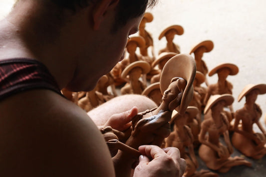 A sculptor hand-shaping terracotta clay figures of the human form in a studio