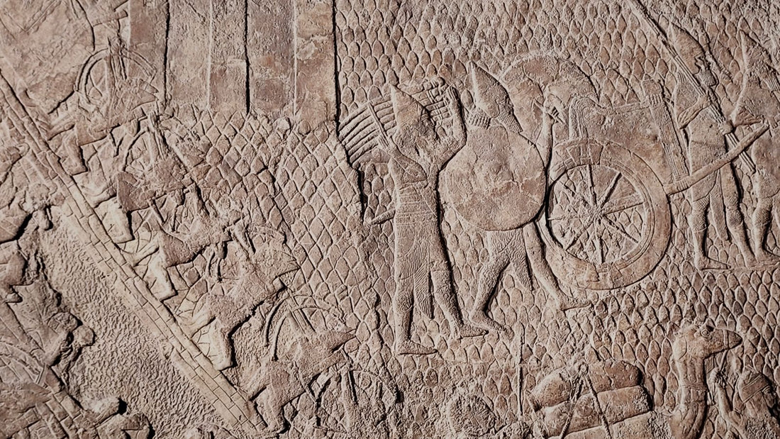 Ancient Assyrian low-relief stone panel showing carved figures, a chariot wheel, and a siege scene