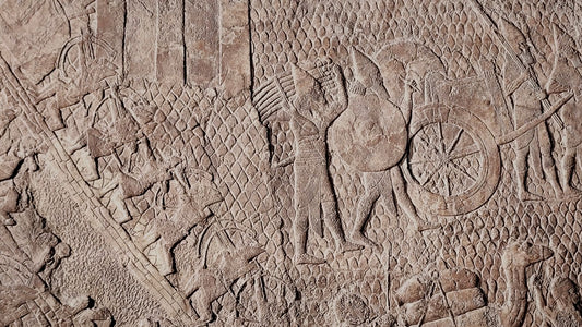 Ancient Assyrian low-relief stone panel showing carved figures, a chariot wheel, and a siege scene