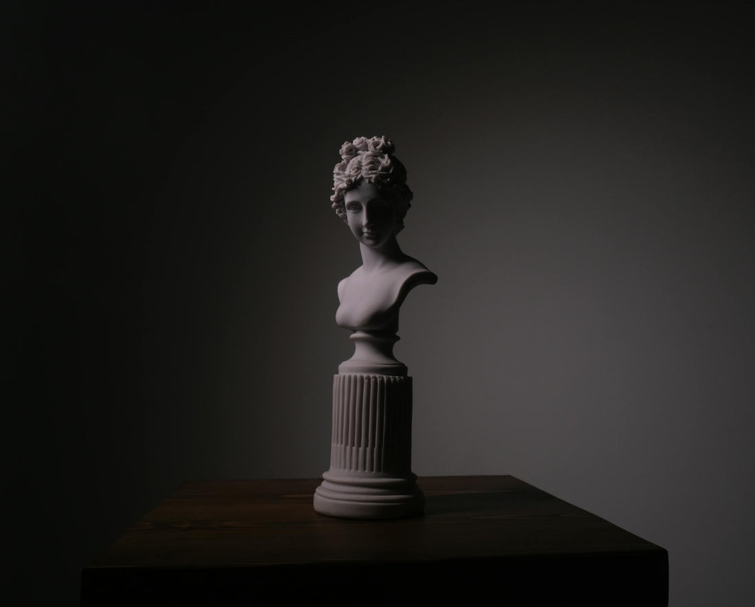 A figurative sculpture lit from above on a dark pedestal in a quiet studio setting