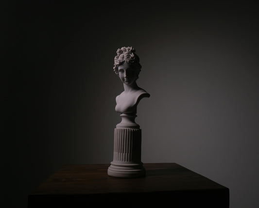 A figurative sculpture lit from above on a dark pedestal in a quiet studio setting