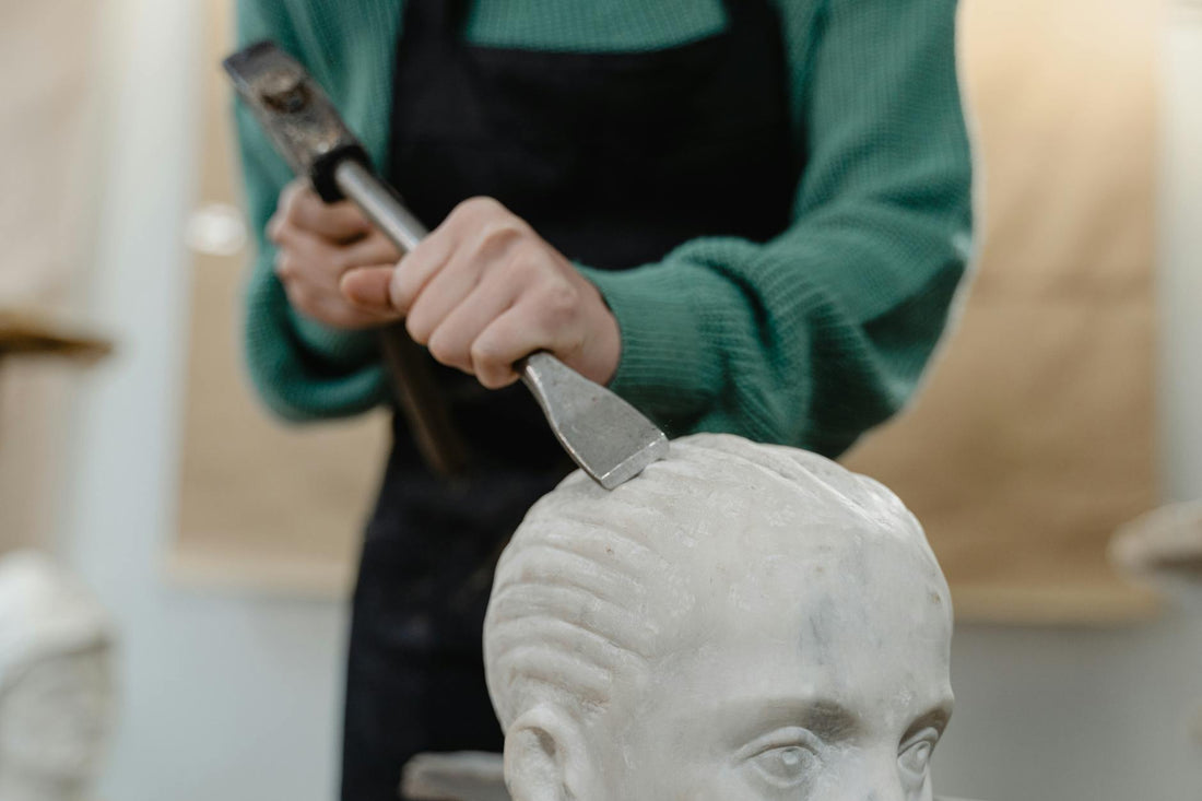 A sculptor carving stone with chisel and hammer in a studio