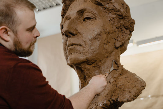 A sculptor shaping a clay bust with a loop tool in a sunlit studio