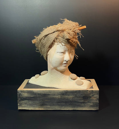 Sculpture of a head with a woven hat and stones on a dark background