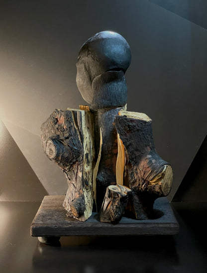 Wooden sculpture of a figure sitting on a log against a dark background