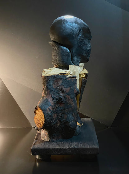Abstract sculpture with a dark gray finish on a black platform against a gray background