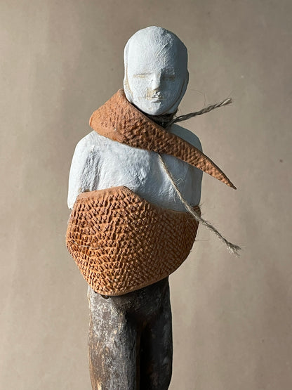A sculpture of a figure with a painted white face and body, with a brown burlap material wrapped around its neck and chest.
