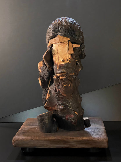 Sculpture of a figure's face on top of a wooden base back side