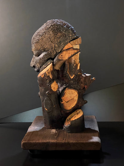 Sculpture of a figure's face on top of a wooden base left side
