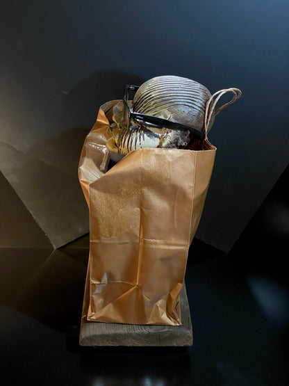 Brown paper bag with a ceramic sculpture on a dark surface
