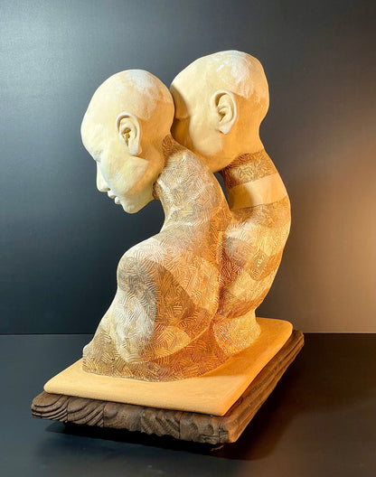 Wooden sculpture of two intertwined figures on a dark surface with a gradient background