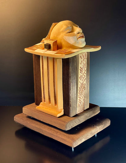 Wooden sculpture of a face on a pedestal with a dark background