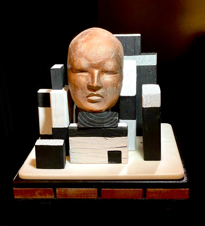 Abstract sculpture with a face-like head and geometric blocks on a dark background