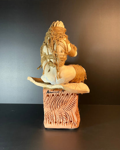 Ceramic sculpture of a seated figure with intricate patterns on a dark background