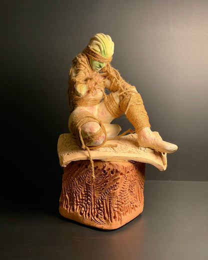Ceramic sculpture of a figure with a textured surface on a dark background