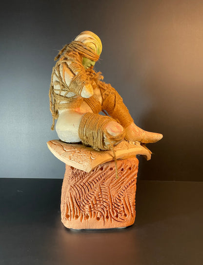 Ceramic sculpture of a figure sitting on a pedestal with a dark background